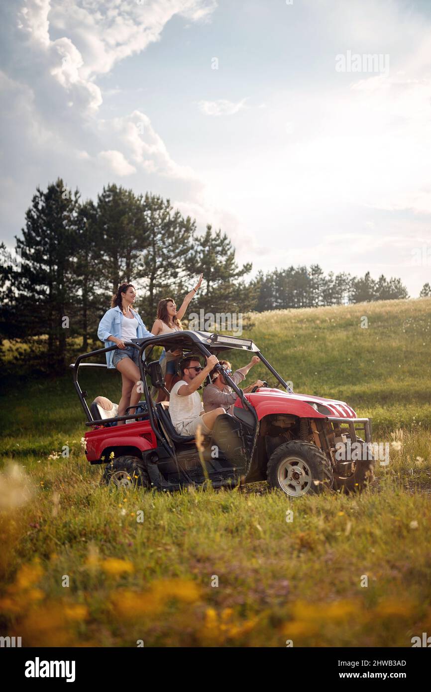 Young happy excited friends enjoying beautiful sunny day while driving a off road buggy car on mountain nature. Freedom, friendship, nature concept. Stock Photo