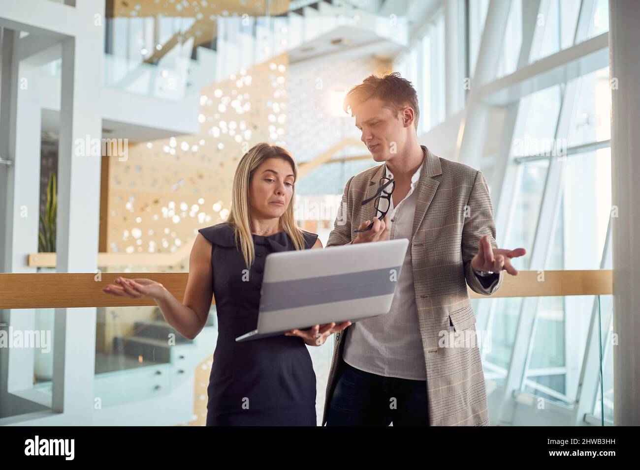 Two young business colleagues having a conversation about laptop content they watching together in a pleasant atmosphere in the hallway. Business, peo Stock Photo