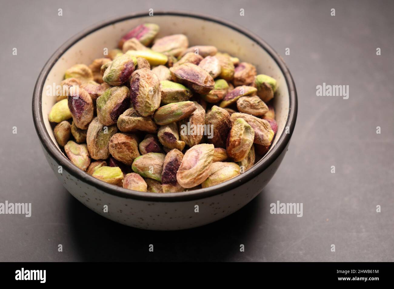 Peeled pistachio nuts in a bowl over black background. Baked pistachios
