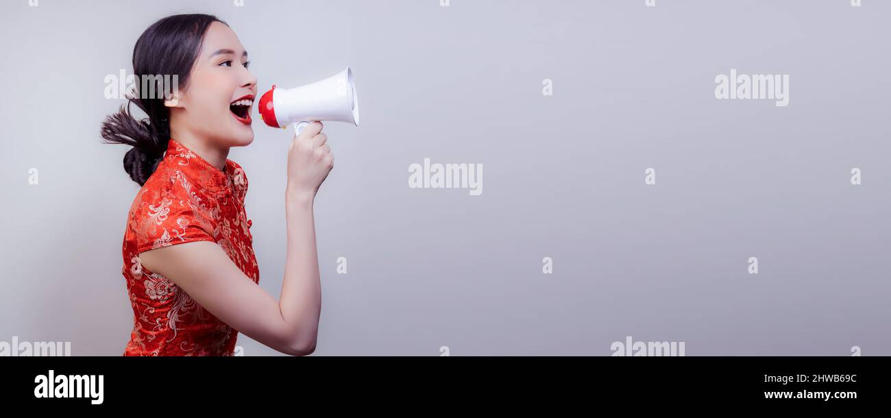 Asian woman in national dress of Chinese new year holding megaphone, shout and inform  big and flash sell in soft isolated background Stock Photo