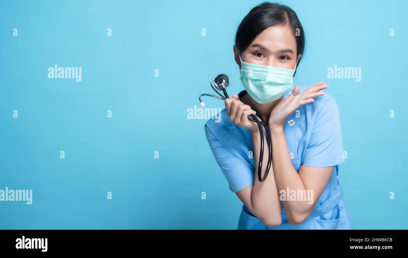 Asian Thai nurse or doctor wearing mask and holding stethoscope with big smiled isolated in studio on blue background Stock Photo