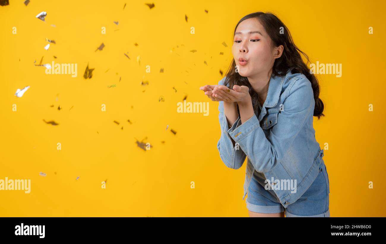 Asian beautiful woman blowing and celebrate, Cute Thai girl blow paper for celebration in studio on yellow background Stock Photo