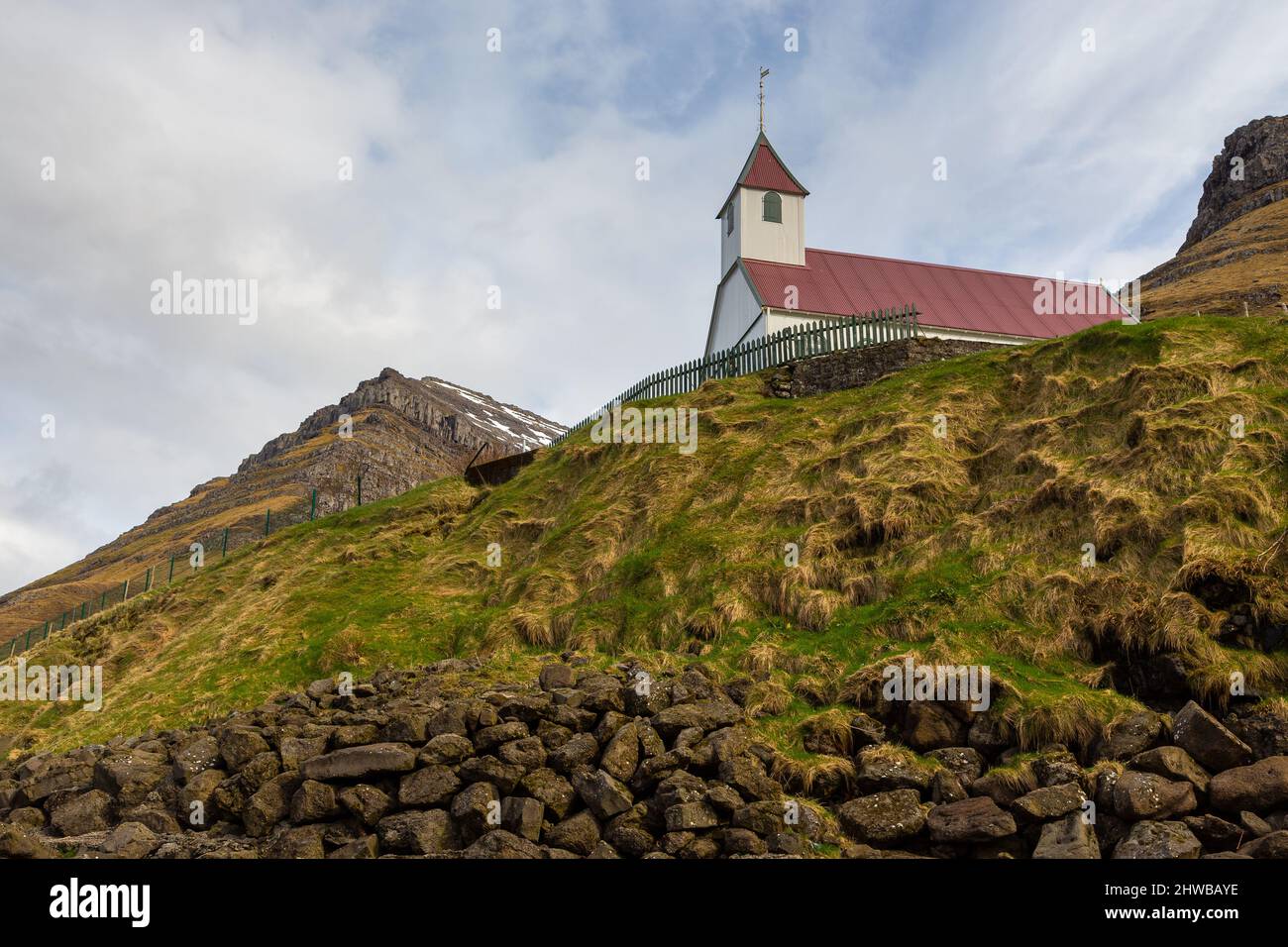 Kunoy Church on a hill. Steep coast of the island of Kalsoy in the background. Kunoy, Faroe Islands. Stock Photo