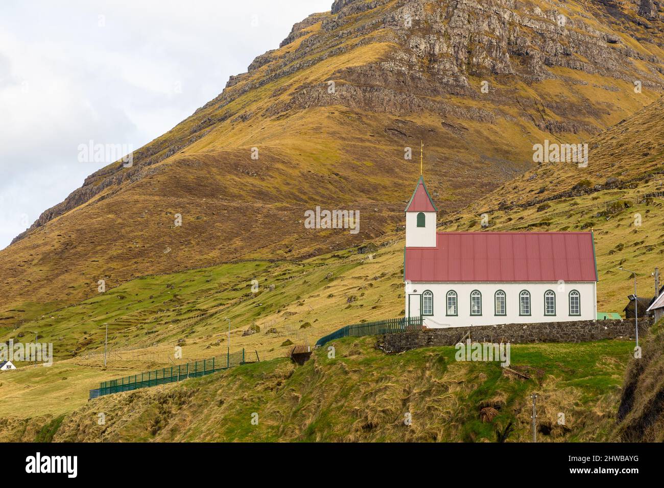 Kunoy Church on a hill. Steep coast of the island of Kalsoy in the background. Kunoy, Faroe Islands. Stock Photo