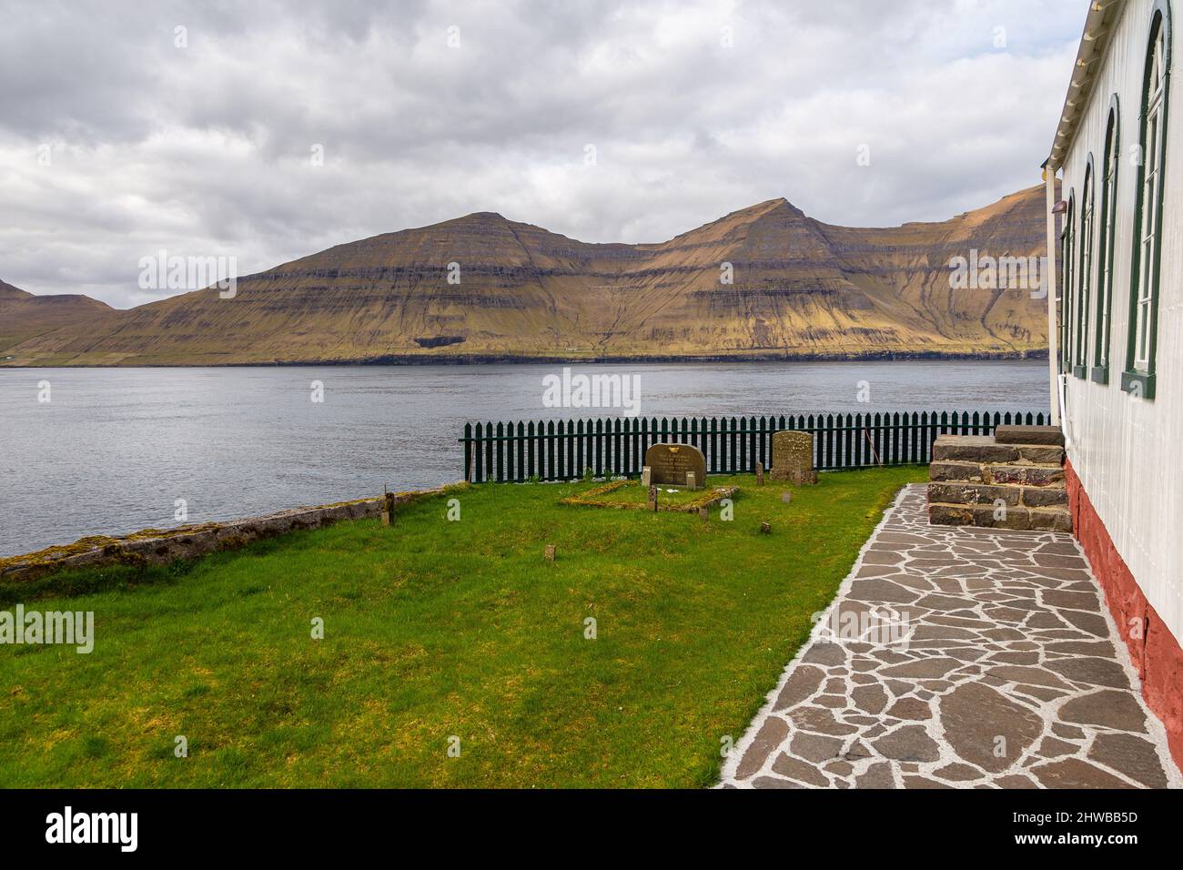 Kunou, Faroe Islands - 02 May 2018: Kunoy Church on a hill. Steep coast of the island of Kalsoy in the background. Stock Photo