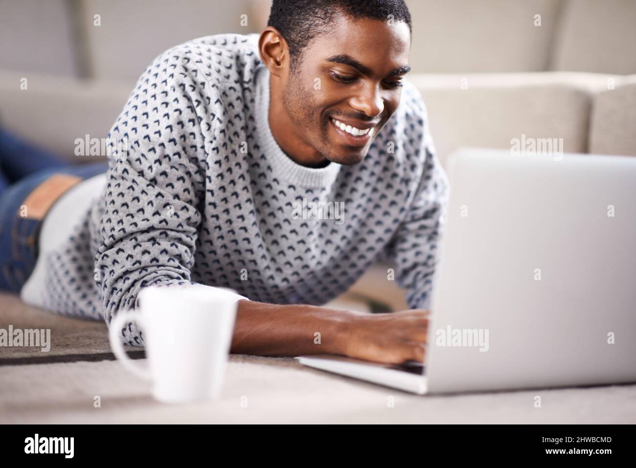 Having coffee with a friend. Cropped shot of a handsome young man using his laptop while relaxing at home. Stock Photo