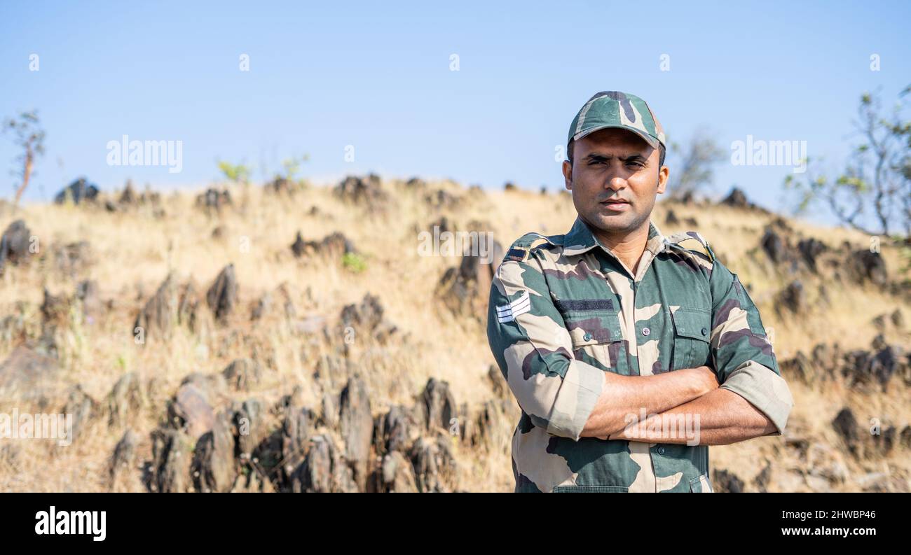 Confident smiling indian soldier in uniform standing with arms crossed by looking at camera with copy space - concept of successful, proud serviceman Stock Photo