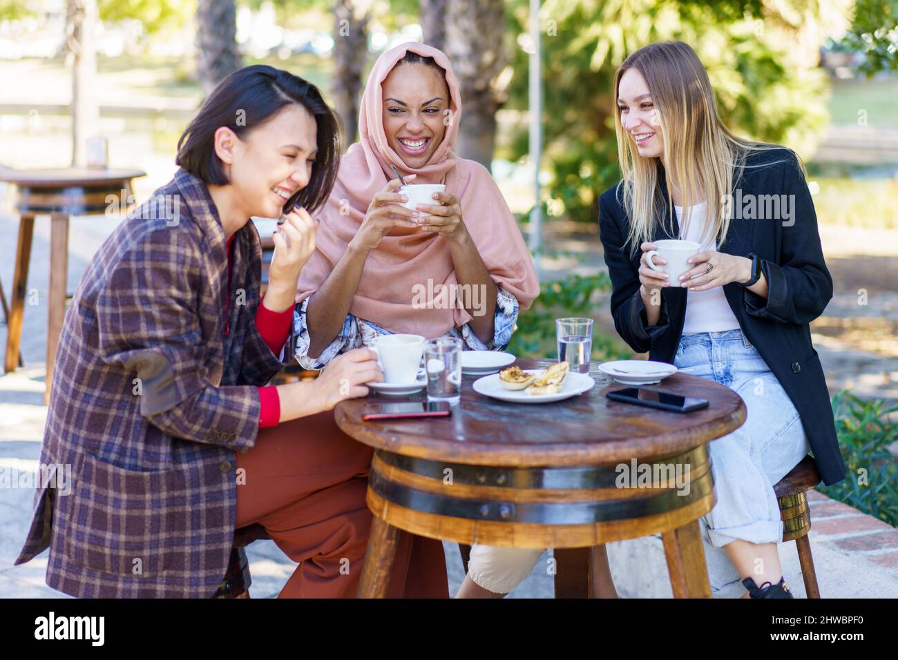 Laughing diverse women having coffee break in outdoor cafe Stock Photo