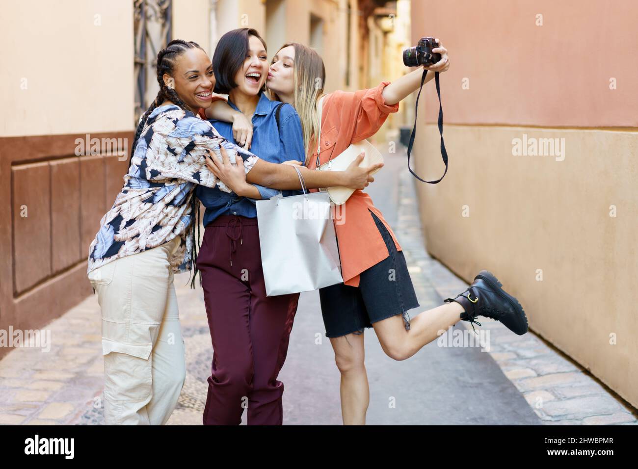 Joyful young diverse women embracing and taking selfie on camera in city Stock Photo