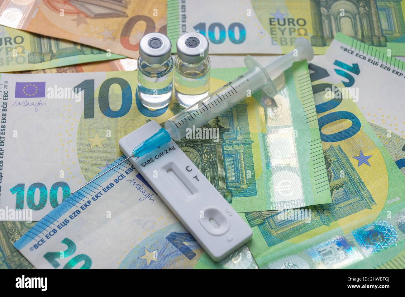 Money (Euro currency banknotes) with medical mask, antigen test, vaccine bottles and syringe. Financial crisis due to Coronavirus losses, selective fo Stock Photo