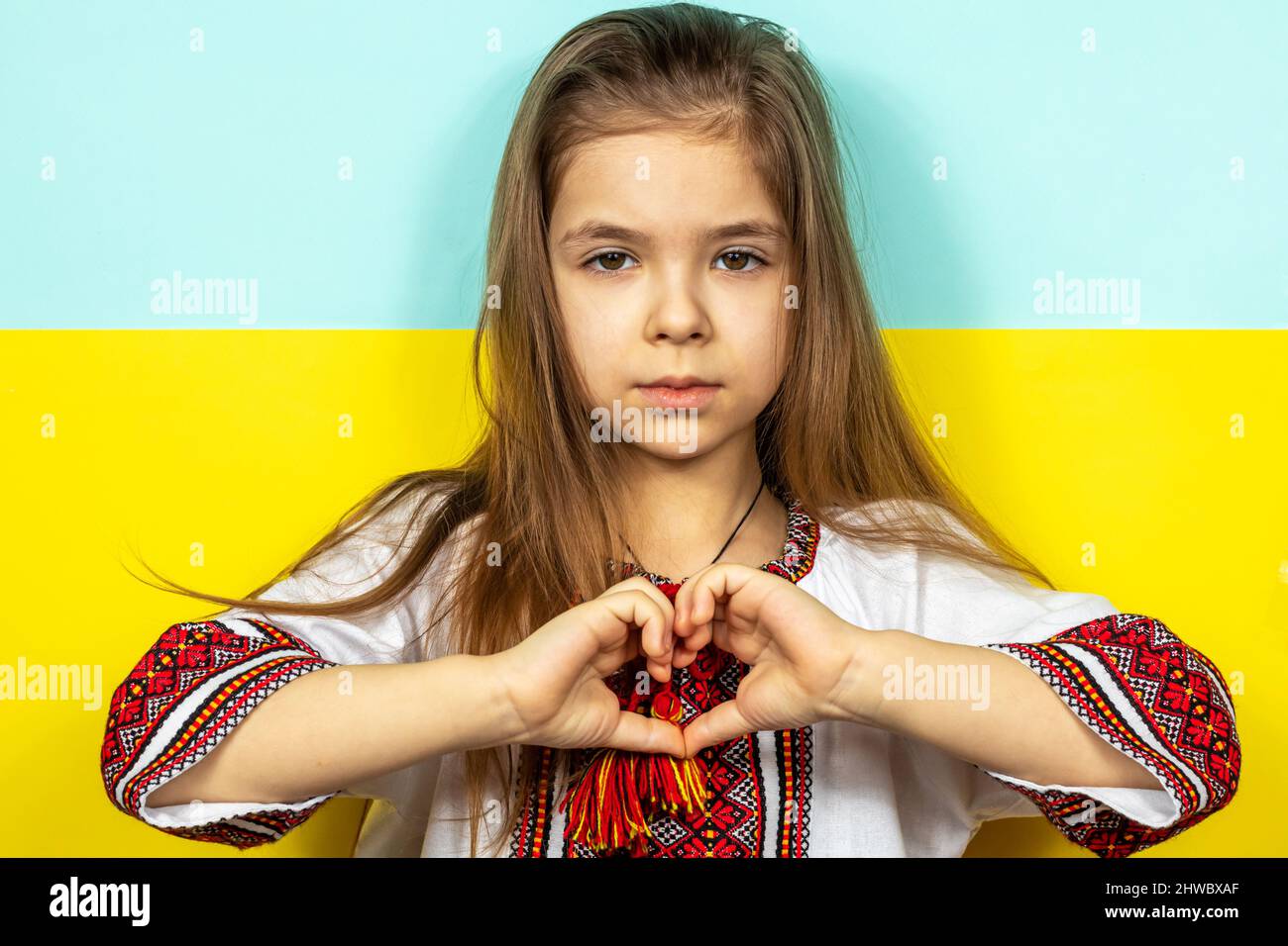 A girl in national Ukrainian clothes, an embroidered shirt, shows a heart sign as a sign of love for Ukraine, close-up against the background of the Stock Photo