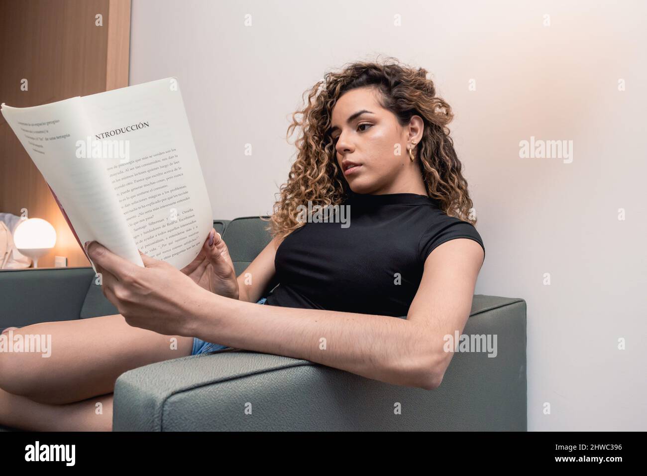 portrait of caucasian young woman in casual clothes resting sitting on the sofa at home turning the page of the book she is reading, lifestyle and rea Stock Photo
