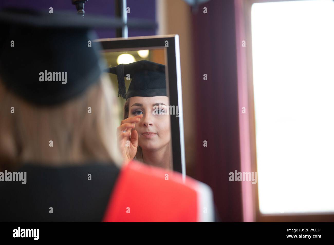 A female European Graduate gets ready for the official photographer at their graduation day ceremony. This formal event where graduands (before) chang Stock Photo
