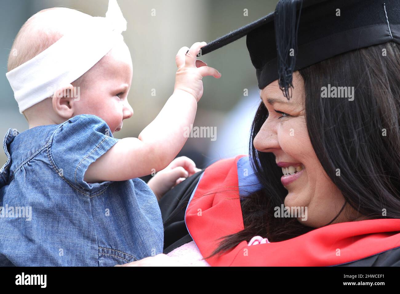 An European mother graduate posing for photographs with her baby daughter at her graduation day ceremony. This formal event where graduands (before) c Stock Photo