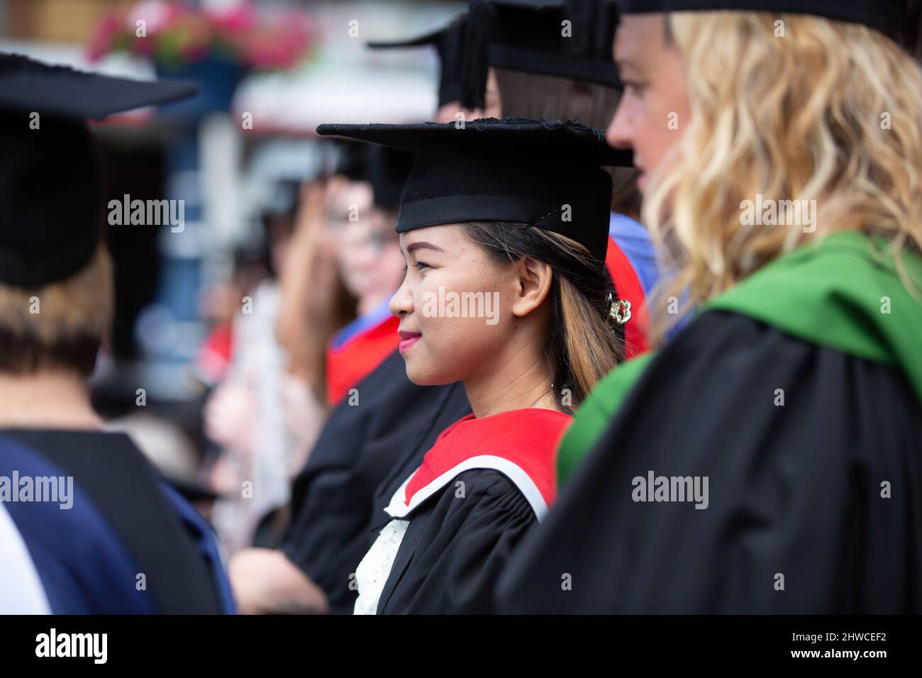 A pretty Asian female graduate lines up with her fellow graduates at her graduation day ceremony. This formal event where graduands (before) change in Stock Photo