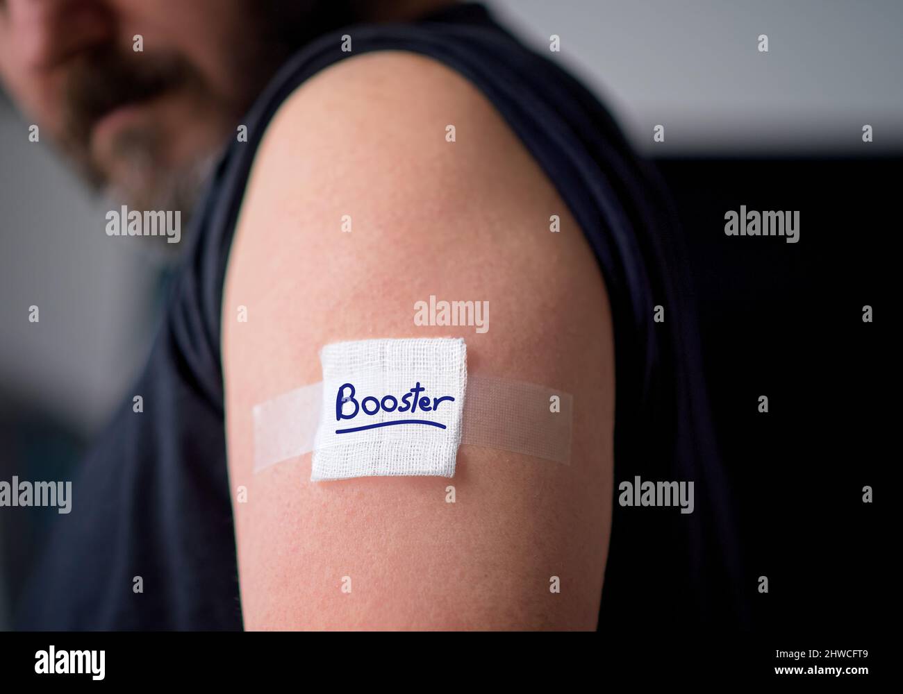 Vaccinated man looking down at plaster bandage on shoulder right after getting covid-19 vaccine shot. Booster shot concept. High quality photo Stock Photo
