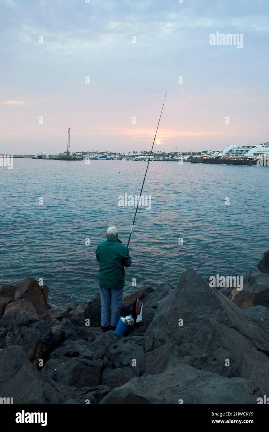 man fishing off the rocks in the sea at sunset playa blanca lanzarote canary islands spain Stock Photo