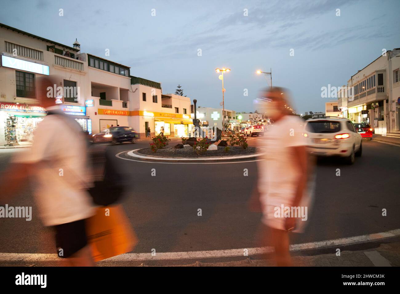 blurred people walking past on a night out roundabout in town centre of playa blanca at night lanzarote canary islands spain Stock Photo