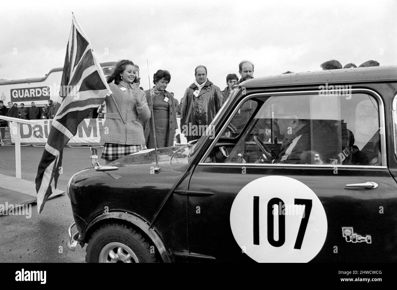 R.A.C. Rally Start: Miss U.K., Sheena Drummond pictured with Union Jack waves off Car No. 107, the blue Austin Cooper S. at the Wheel is co-driver John Miles: in the passenger seat is Sunday Mirror entrant Mark Kah. November 1969 Stock Photo