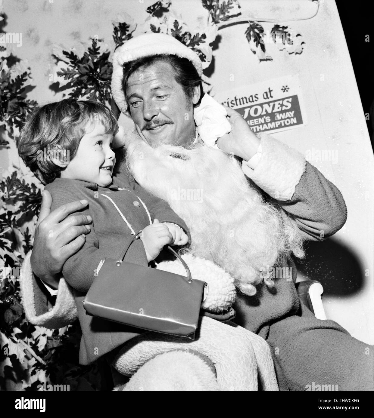 Roger Moore in Southampton for a preview of his latest film 'Crossplot' popped into a local department store to look at the Christmas Scene. He said he always wanted to be a Father Christmas and listened to some of the children's wants for delivery on Christmas Morn. Roger Moore with Melanie Ingham,4 (left) and Anna Maria Devine,4.  November 1969  Z11380-001 Stock Photo