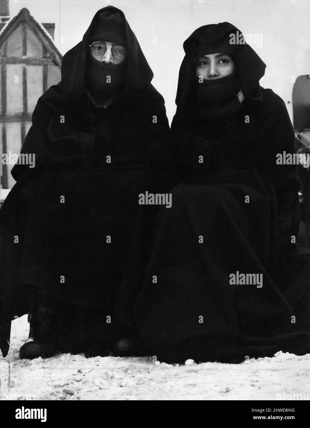 John Lennon of The Beatles pop group pictured with his wife Yoko Ono taking part in another happening. In the snow covered village of Lavenham, Suffolk, they re-enacted a scene from their latest film 'Apotheosis'. Dressed in long, dark robes and wellingtons, they sat in the square for three hours watching a giant balloon being inflated before they could tart work.The film is the Beatles first attempt at making a wide screen colour film. 6th December 1969. Stock Photo