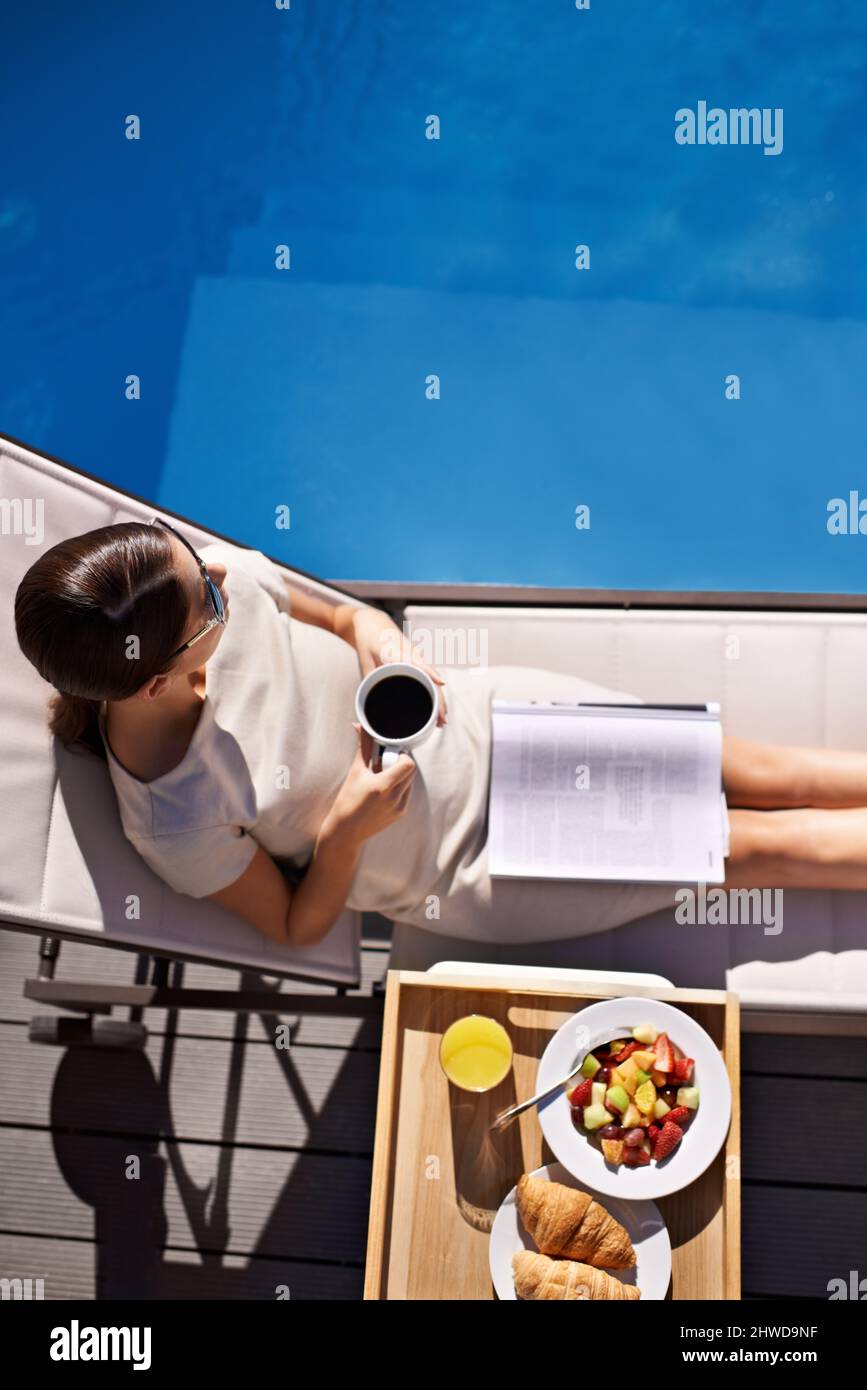 View on luxury. Top view of an attractive young woman enjoying her breakfast by the pool. Stock Photo
