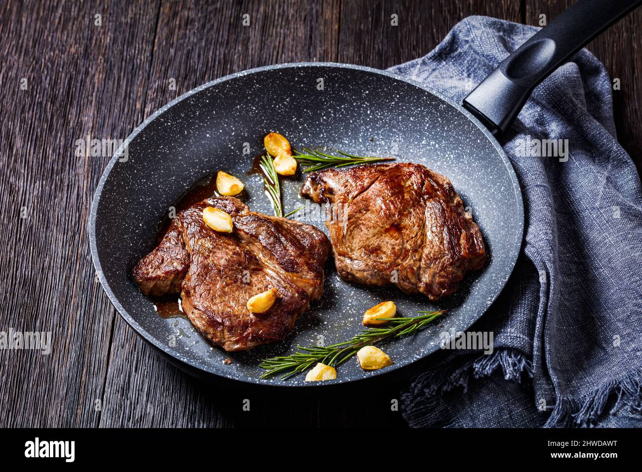 fried chuck eye beef steaks on a skillet with fried garlic cloves and