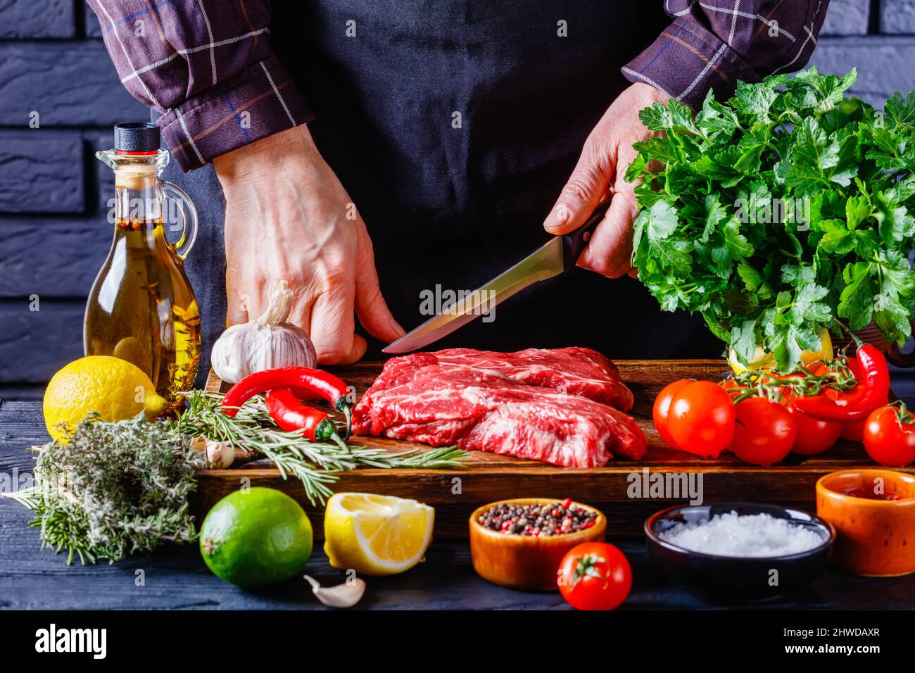male chef is cutting chuck eye beef steak on restaurant kitchen Stock