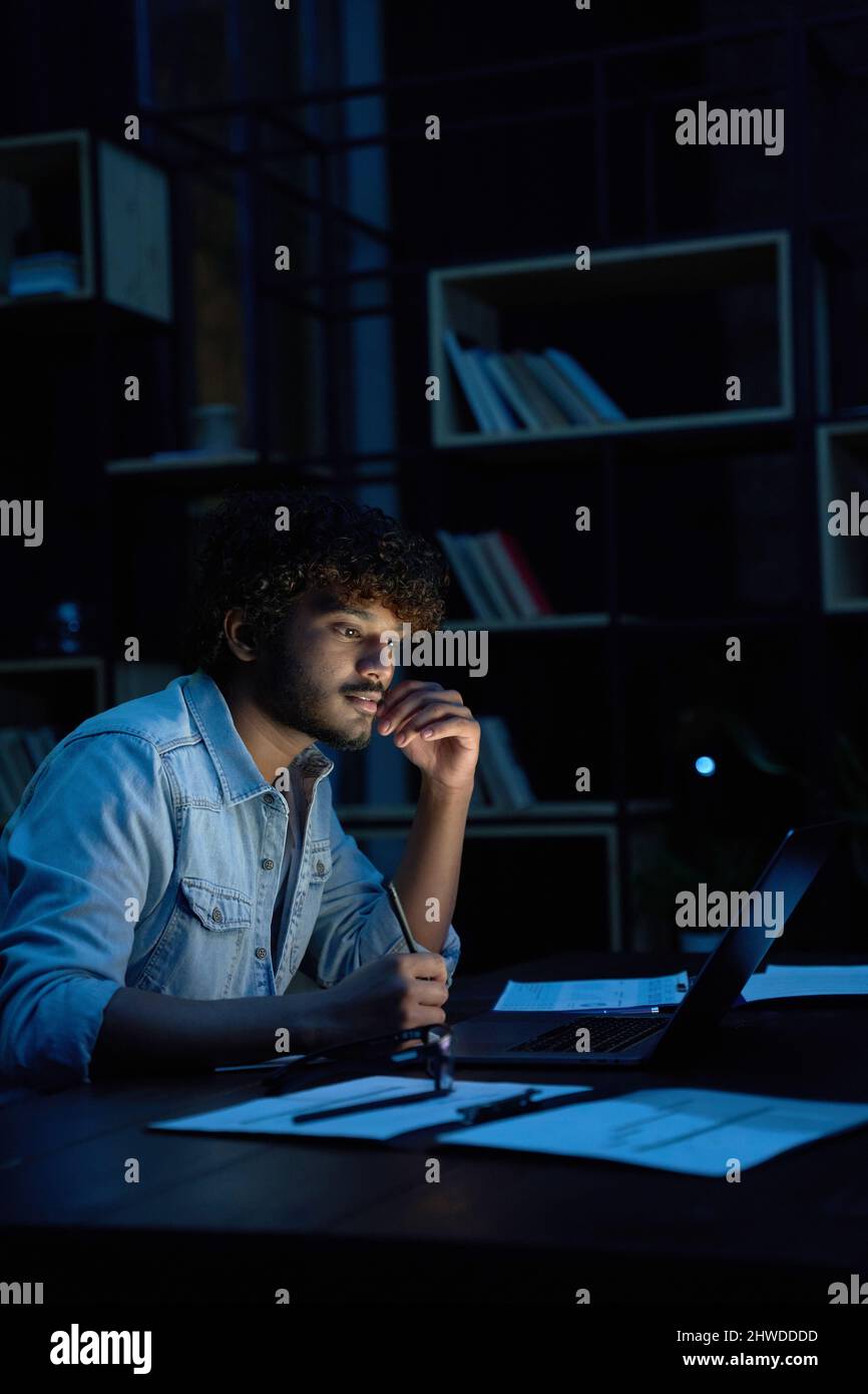 Focused young indian business man working online at night using laptop. Stock Photo