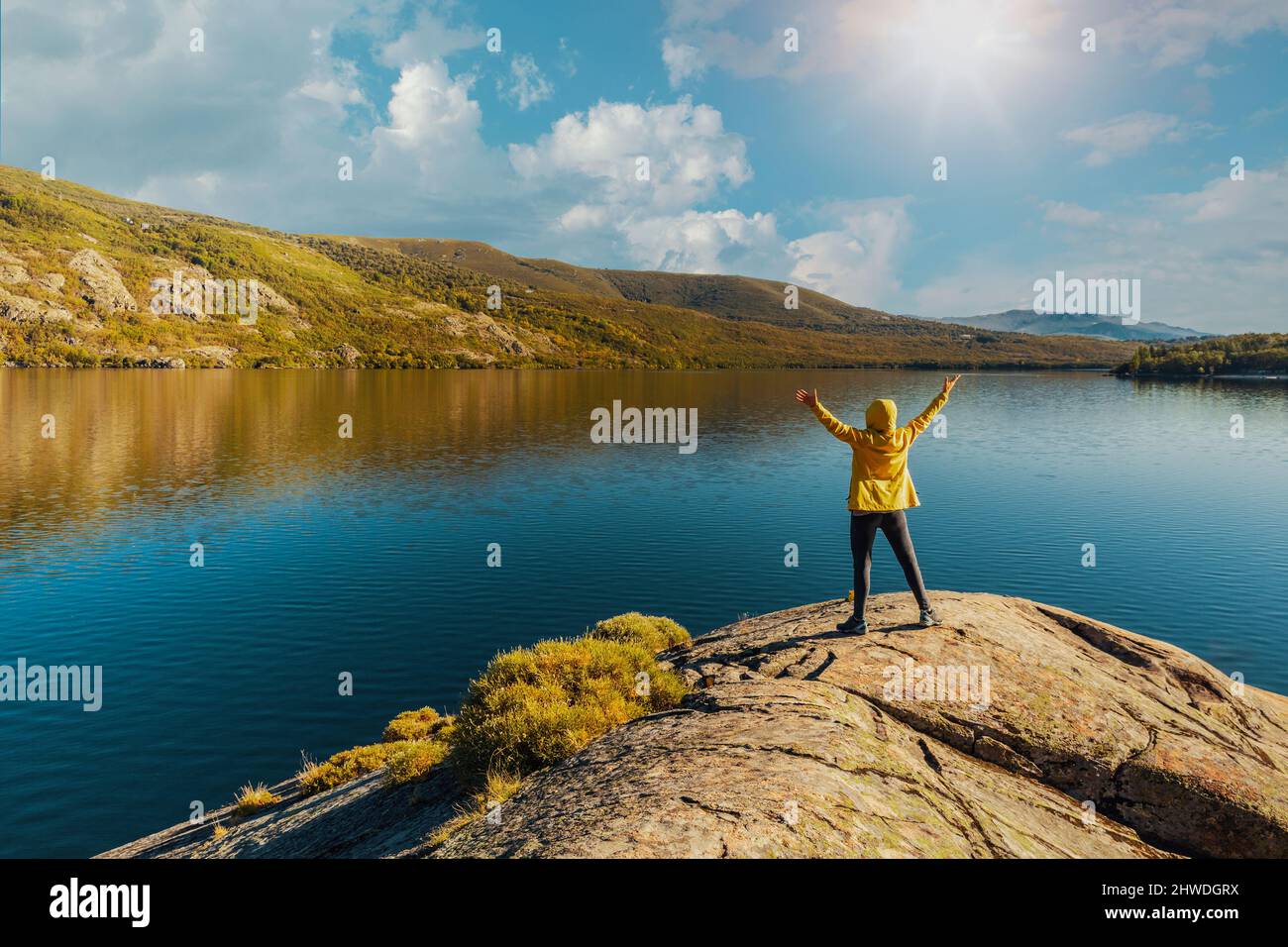 Shot of a woman hiking near a beautiful lake with arms raised Stock Photo