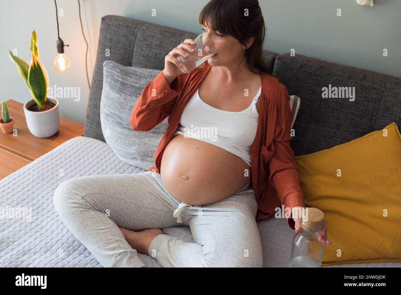 Pregnant woman holding glass of water relaxing in bed at home Stock Photo