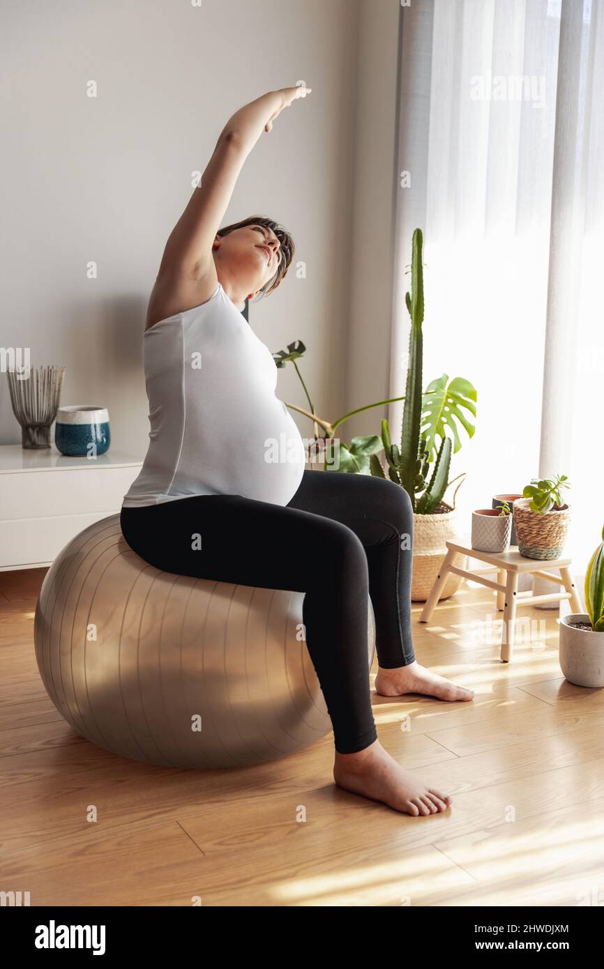 Pregnant woman working out at home doing stretching exercises. Keeping ...