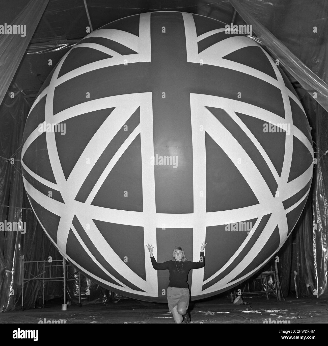 Union Jack Giant Balloon at Expo 70 Pretty receptionist, 23 year old Lynne Roberts, attempts a Charles Atlas pose beneath one of the huge balloons destined to fly over the British pavilion at the Expo 70.   The exhibition will open at Osaka, Japan in March 1970.  The balloon is 20 feet in diameter  Lynne is employed by Loyne Limited, of Ashton under Lyne, Lancashire, where the balloons are being given a special flexible type of coating.  Picture taken 31st December 1969 Stock Photo