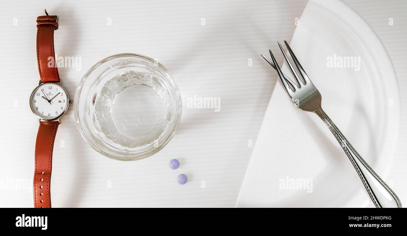 A watch, a glass of water, pills, half a dish and a fork with crooked teeth.. Stock Photo