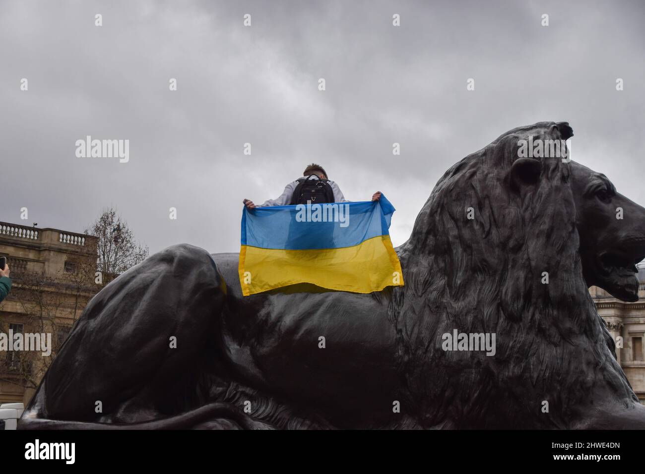 London, UK. 5th March 2022. A protester sits on a lion statue with a Ukrainian flag. Thousands of people gathered in Trafalgar Square for the eleventh day of protests, as the Russian attack on Ukraine continues. Credit: Vuk Valcic/Alamy Live News Stock Photo