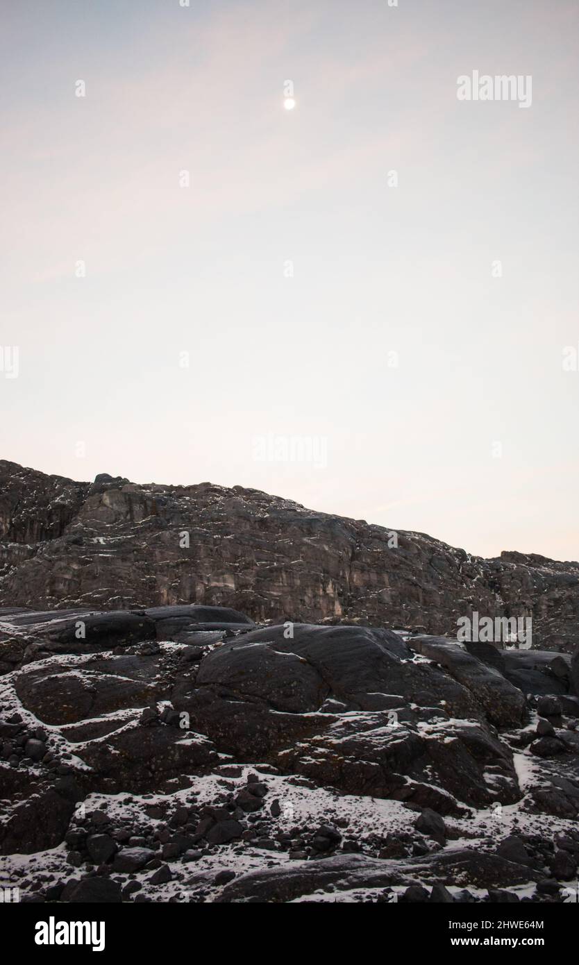 Majestic vertical blue hour landscape of snow, rocks, a ridge and the moon Stock Photo