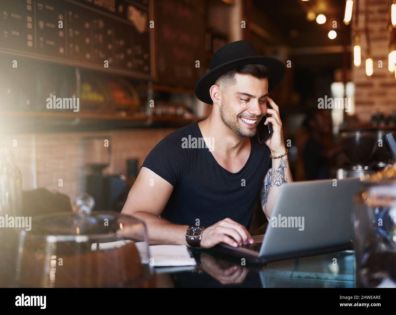 In the coffee industry, the best go wireless. Shot of a young man using a phone and laptop while working in a coffee shop. Stock Photo