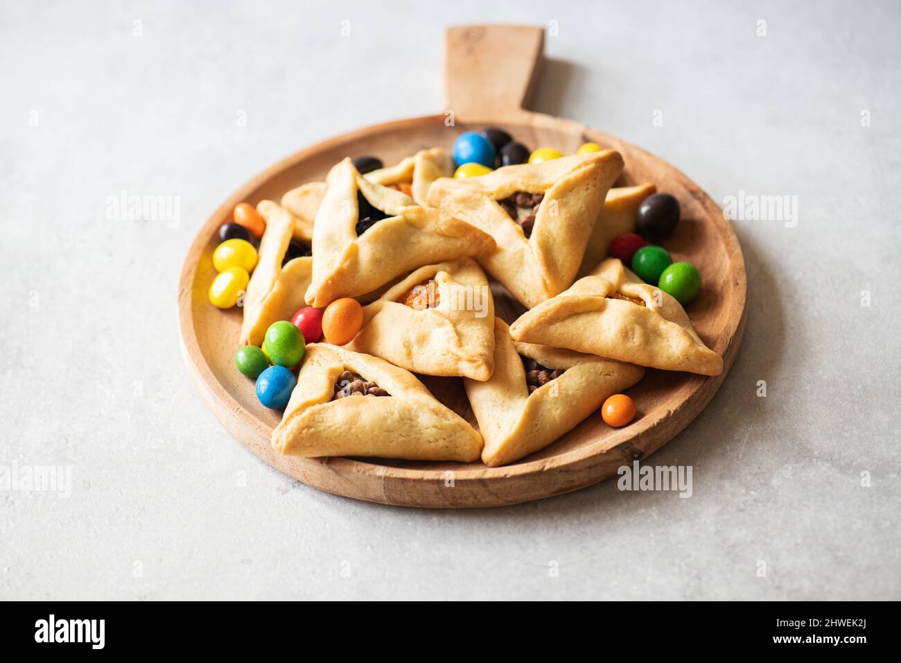 Assorted hamantaschen cookies and colorful candies on a wooden board on a gray background. Copy space. Stock Photo