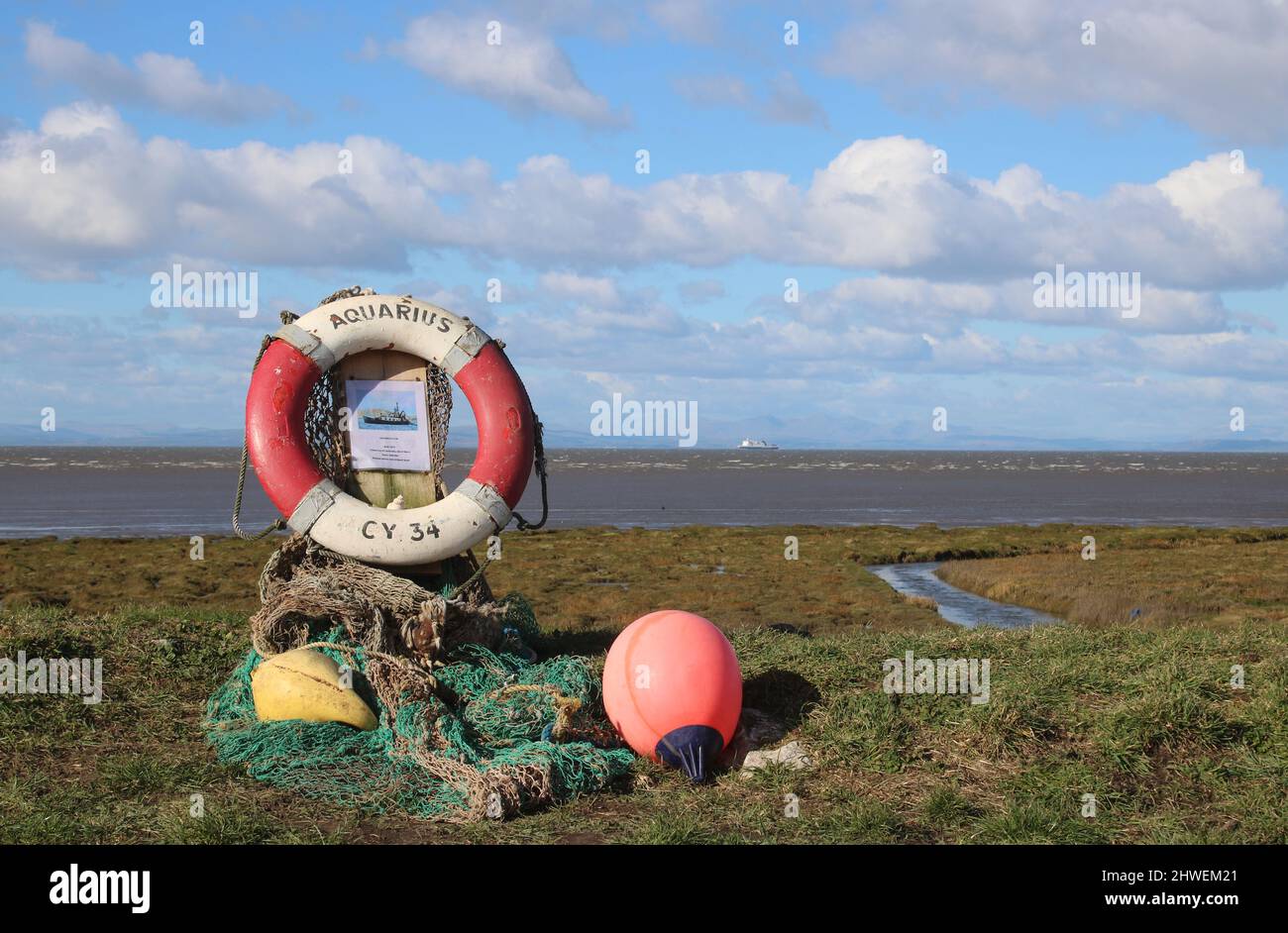 Small collection of assorted objects, lifebelt, buoys, fishing net, information poster on sea wall, Preesall, remembering fishing boat Aquarius CY34. Stock Photo