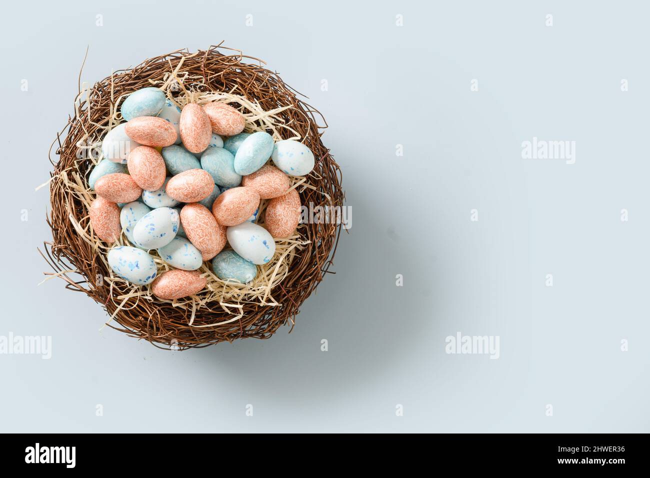 Easter colorful chocolate eggs in decorative nest isolated on blue background. View from above. Flat lay. Space for text. Stock Photo