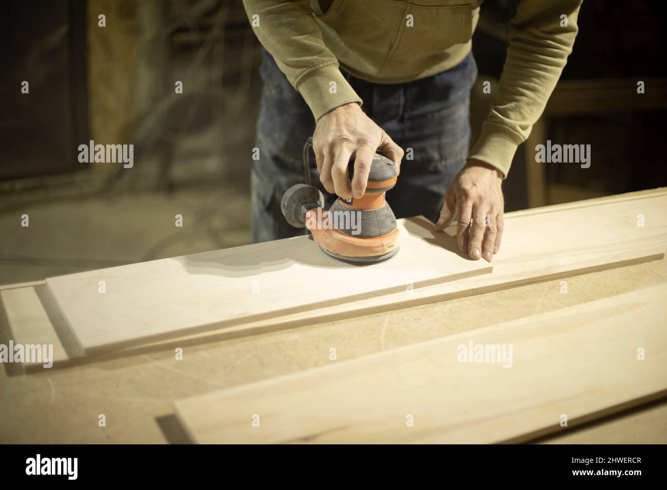 Carpenter grinds wood. Grinding tool. Guy in workshop handles board. Person holds grinding technique in his hands. Stock Photo