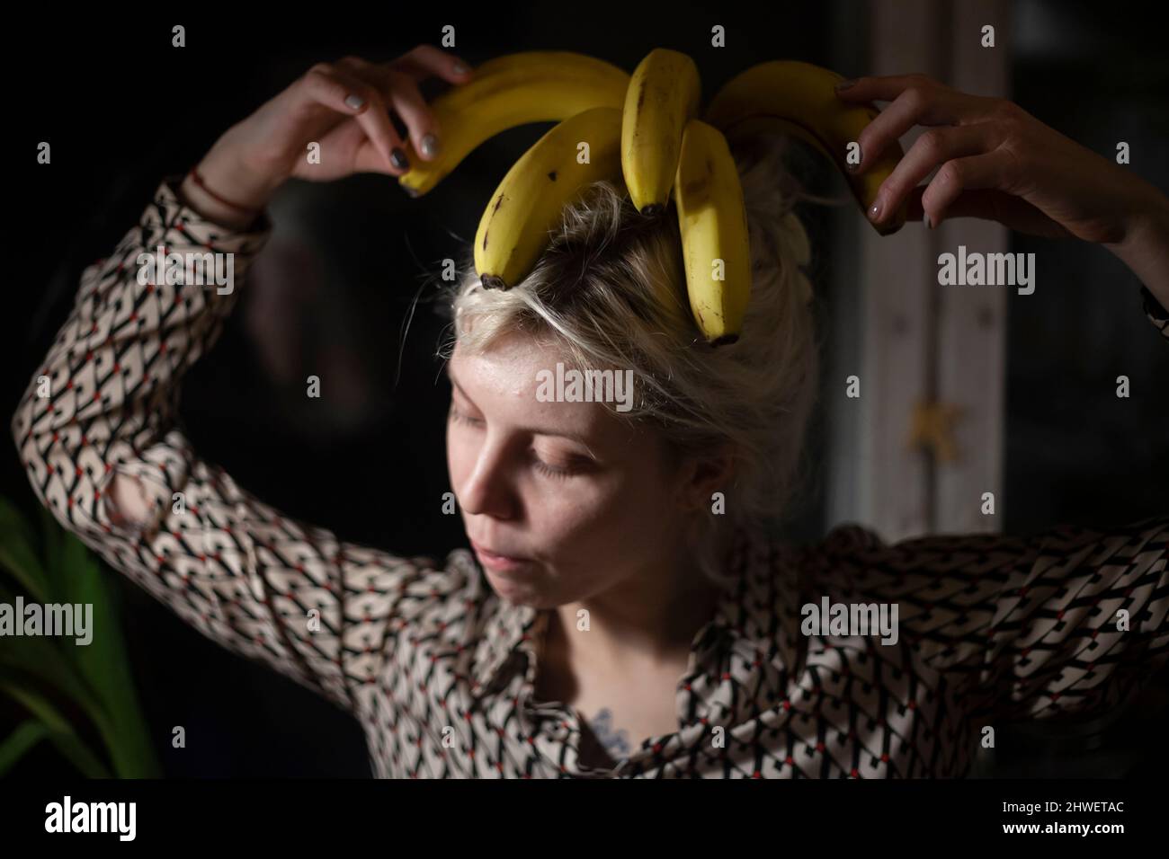 Girl with bananas on her head in the dark. Defiant behavior of young women. The original