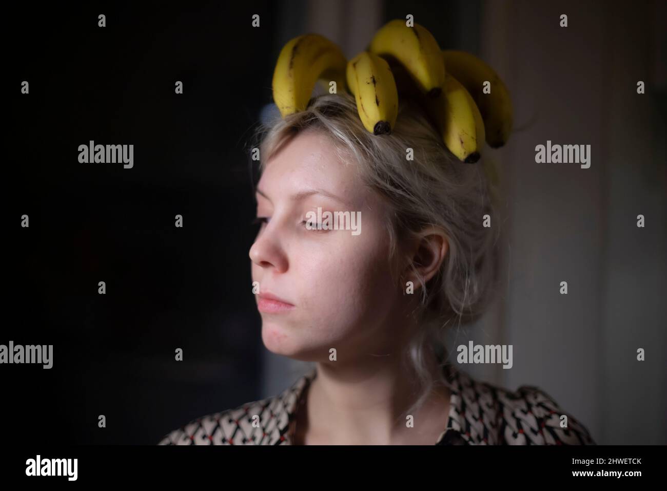 Girl with bananas on her head in the dark. Defiant behavior of young women. The original