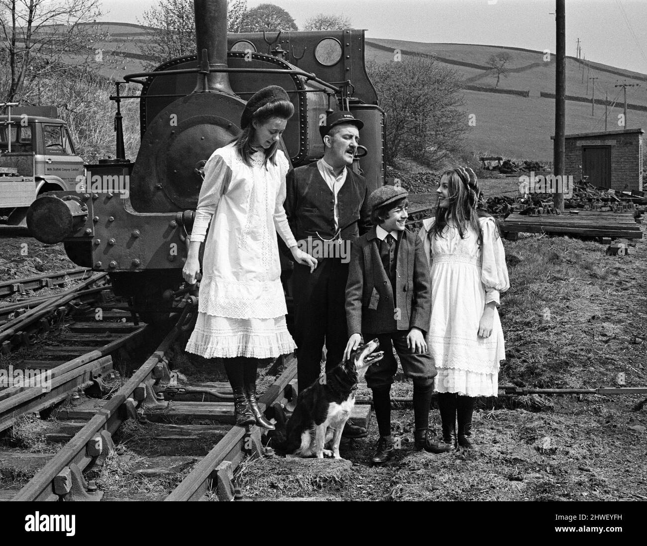 The cameras rolled, the scene was set and the action began when along came Shep. The collie sat in the middle of the track as 'The Railway Children' was being filmed at Haworth, Yorkshire. After being coaxed away the dog was watched by the local Police Sgt. Pictured are Jenny Agutter, Bernard Cribbins, Gary Warren and Sally Thomsett with the dog. 11th May 1970. Stock Photo
