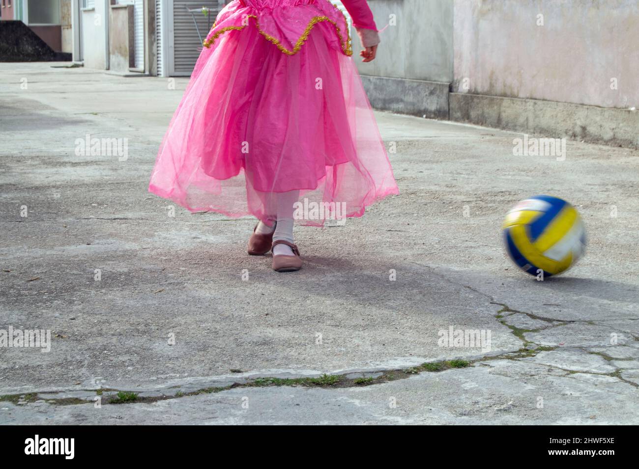 Little girl dressed like a princess playing with a ball. Girls and sports, girls education. Playing outdoor. Girls playing like boys. Stock Photo