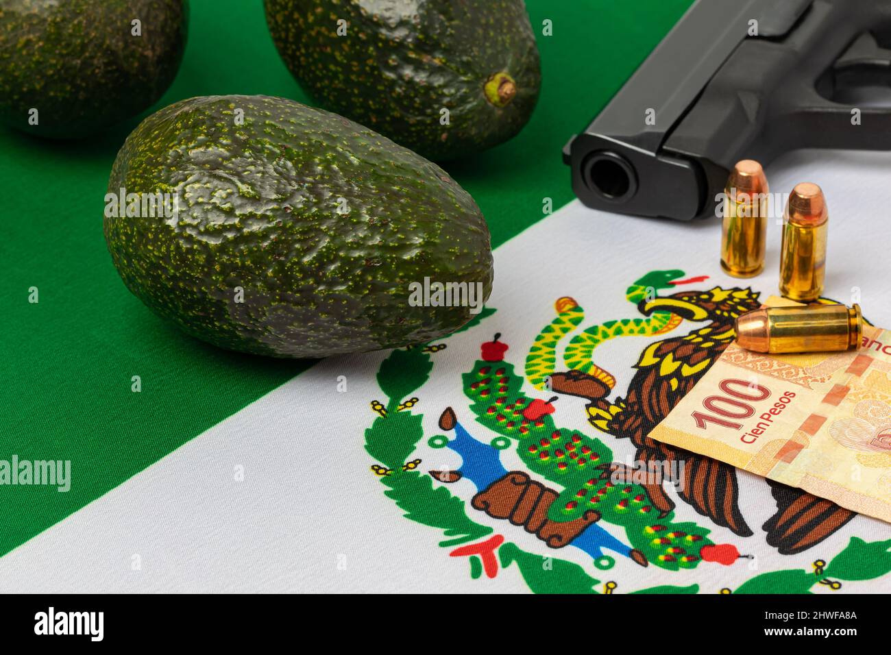 Avocados, Mexico flag and gun. Mexican drug cartel extortion, violence and crime in avocado farming. Stock Photo