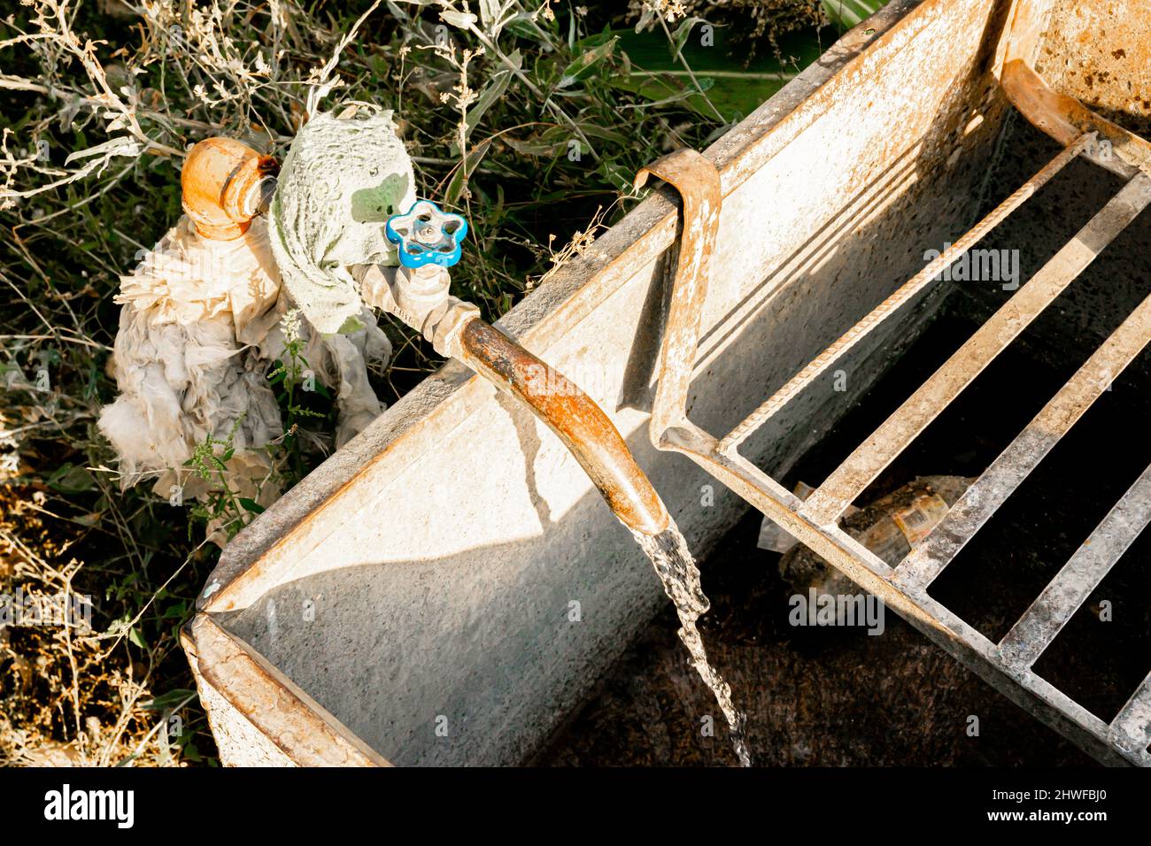 Do-it-yourself DIY garden rustic water faucet filling the concrete reservoir. Water supply used extensively in countryside in USSR/ Russia Stock Photo