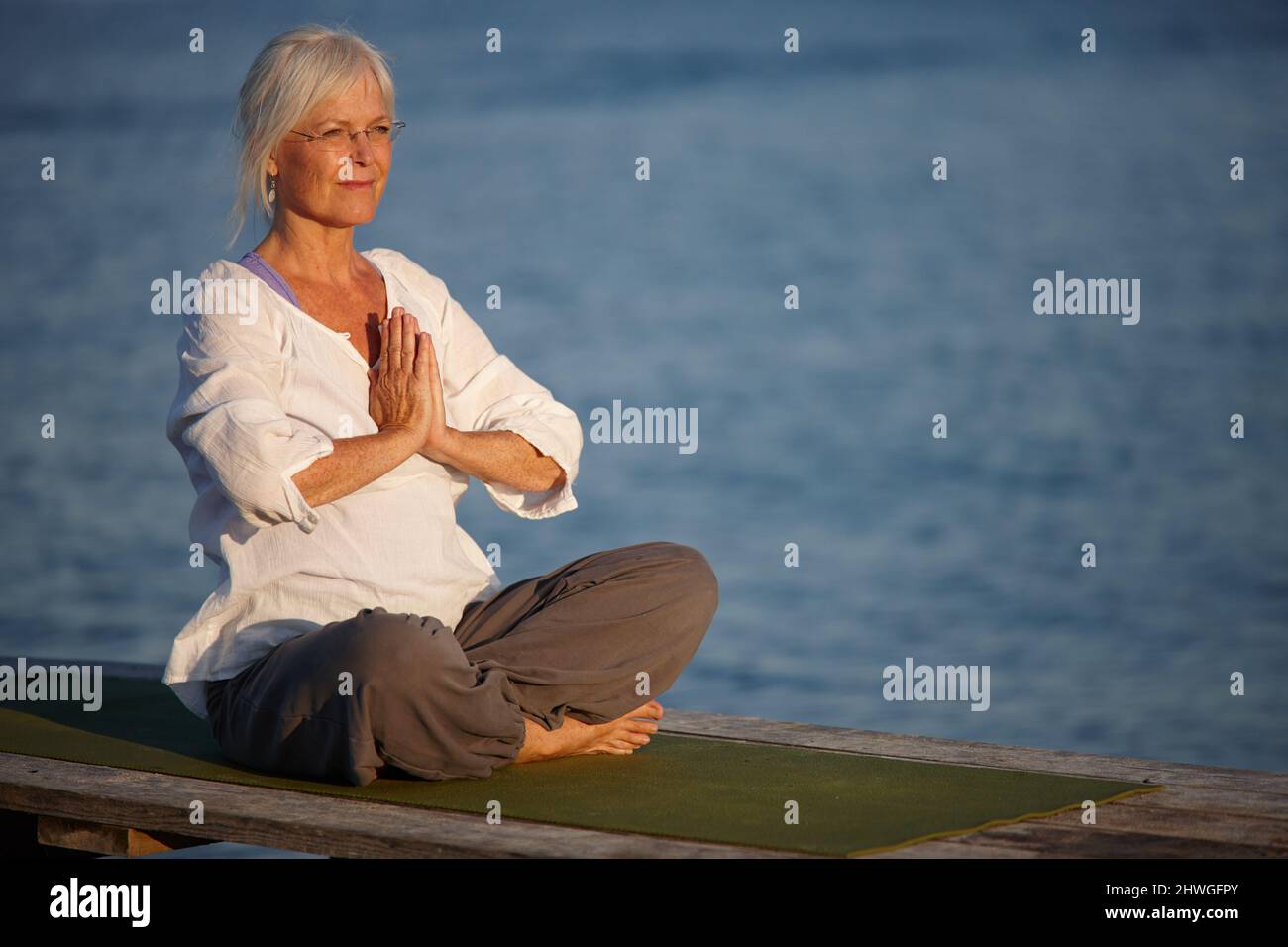 Tranquility by the ocean. Shot of an attractive mature woman doing yoga on a pier out on the ocean. Stock Photo