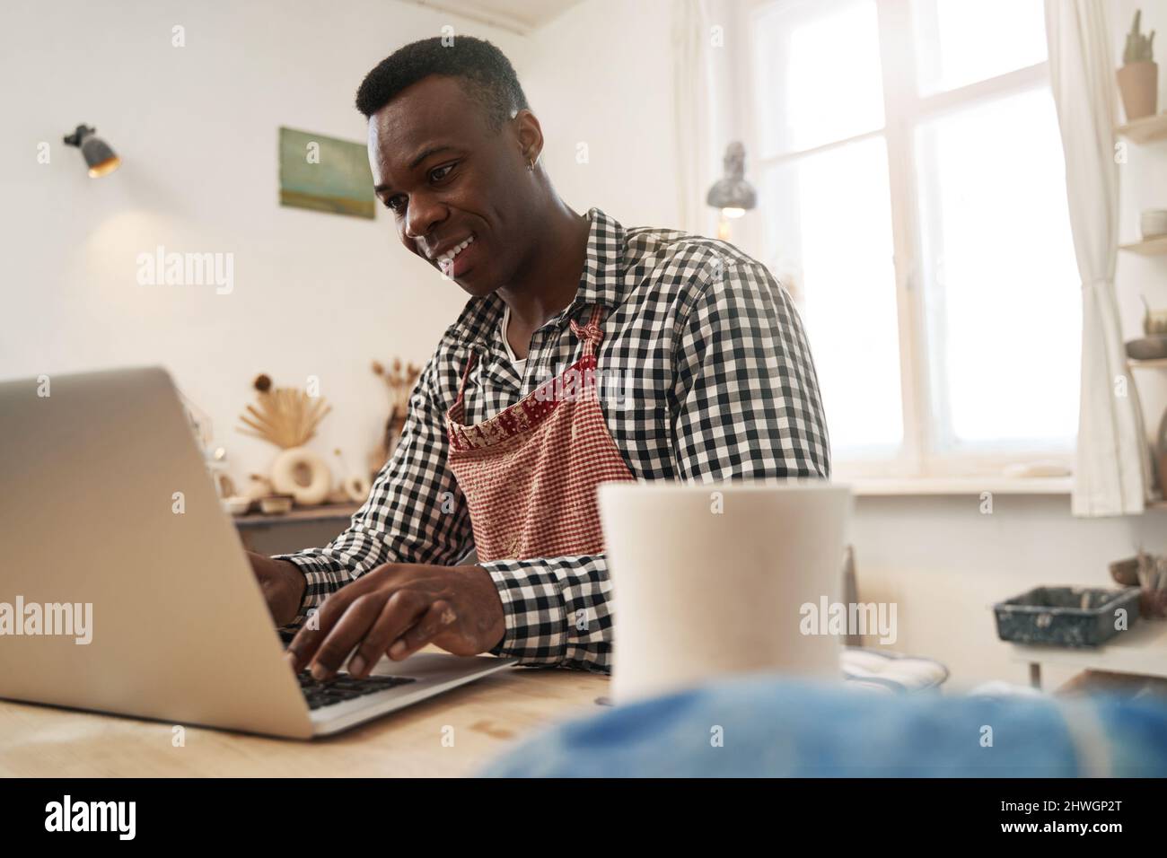 Joyous potter working on laptop in studio Stock Photo