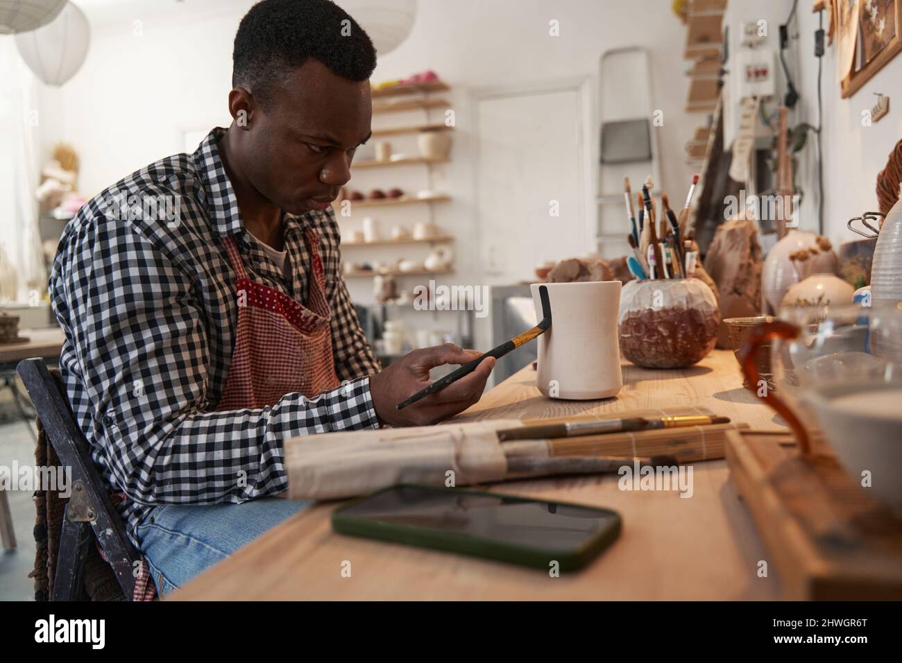 Concentrated young ceramic artist painting unglazed pottery Stock Photo